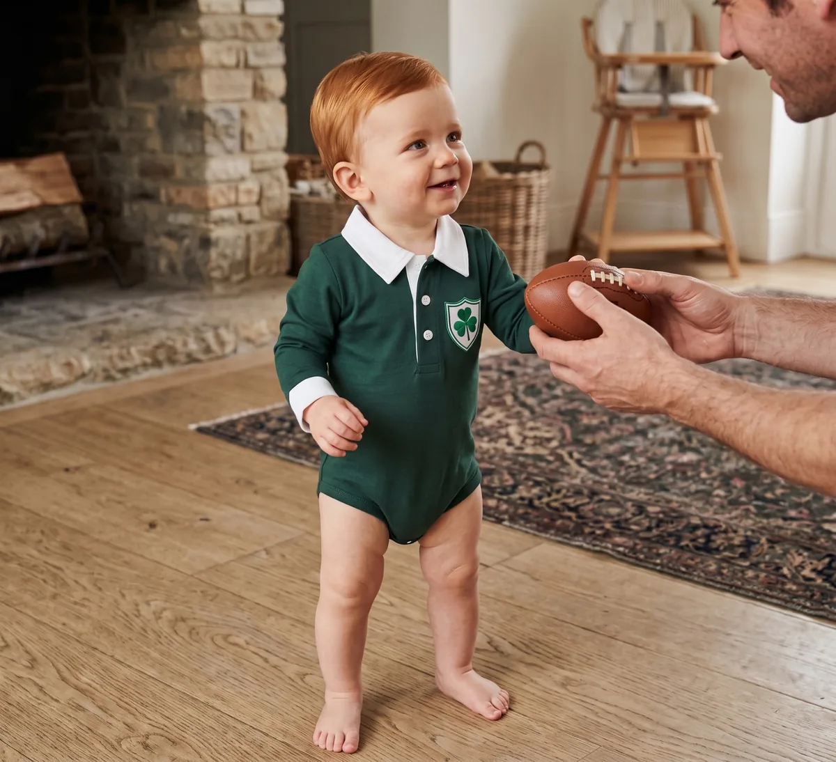A baby wearing the deep green Ireland rugby romper while reaching for a toy rugby ball